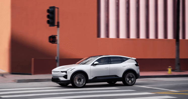 Vit Polestar 3 elektrisk SUV i rörelse på en stadsgata med en stor orange vägg i bakgrunden i Helmia