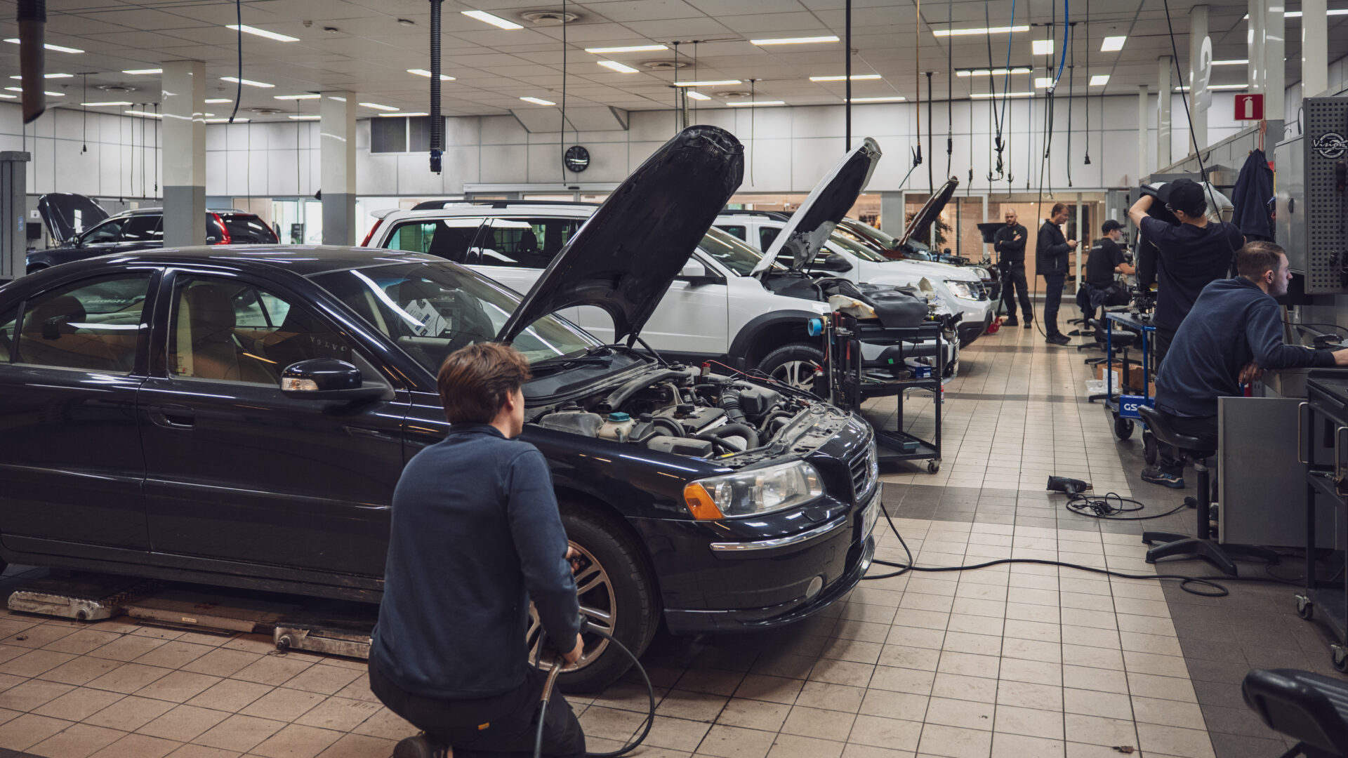 Mekaniker från Helmia arbetar på en svart Volvo med öppen motorhuv i en ljus och välordnad bilverkstad i Arvika