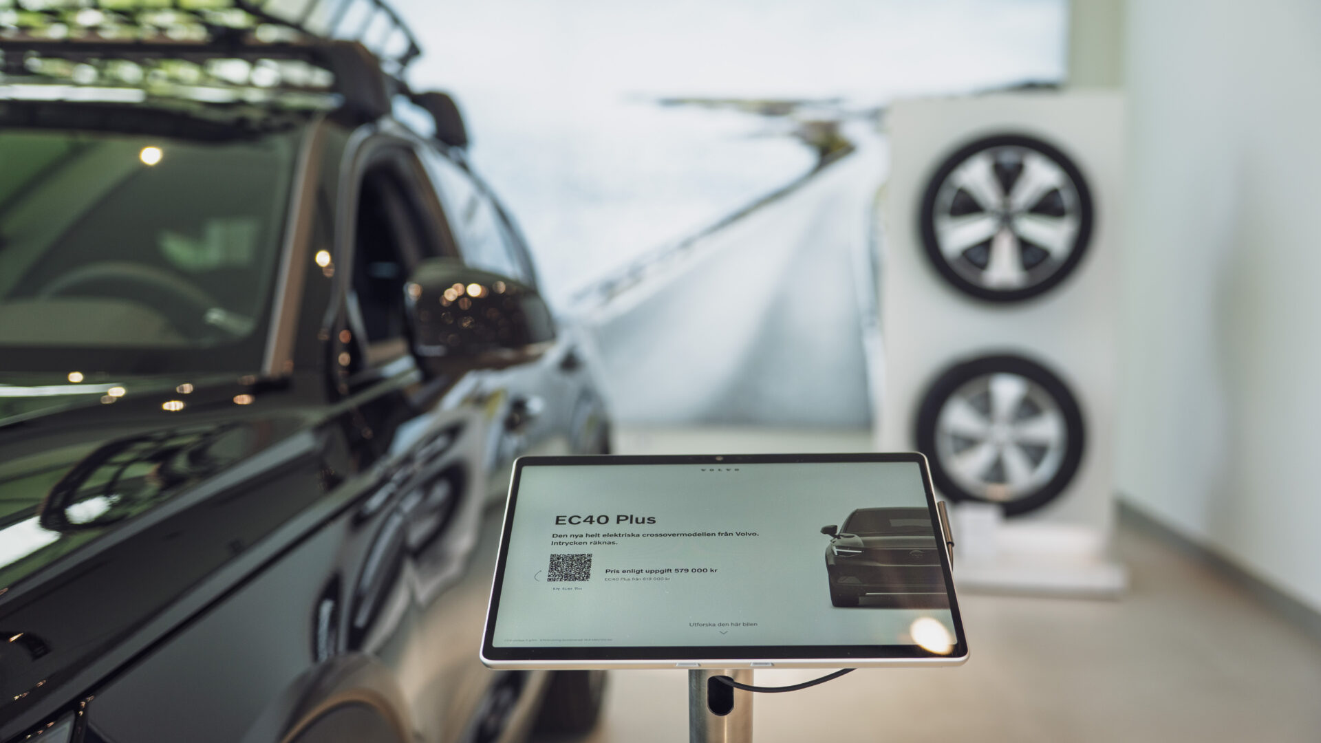 Närbild på en interaktiv digital skärm som visar information om Volvo EC40 Plus elbil i Helmia Bilhall i Arvika, med en del av bilen synlig bredvid skärmen.