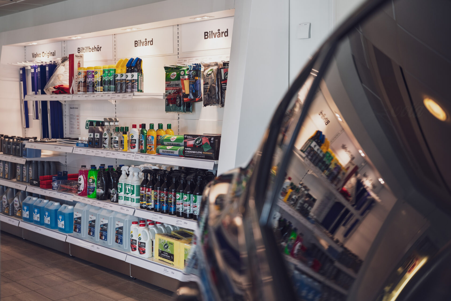 Helmia butik i Karlstad med bilvårdsprodukter och Volvo Original på hyllor speglade i en blank bil