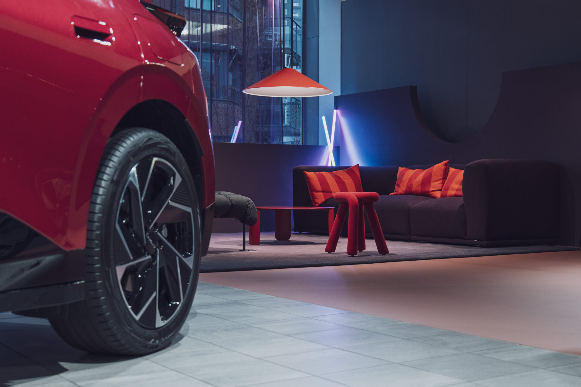 Delvis bild på ett rött Lynk & Co bildäck i en modern inredning med mörk soffa, röda kuddar och minimalistiska röda möbler med mjuk belysning hos Helmia