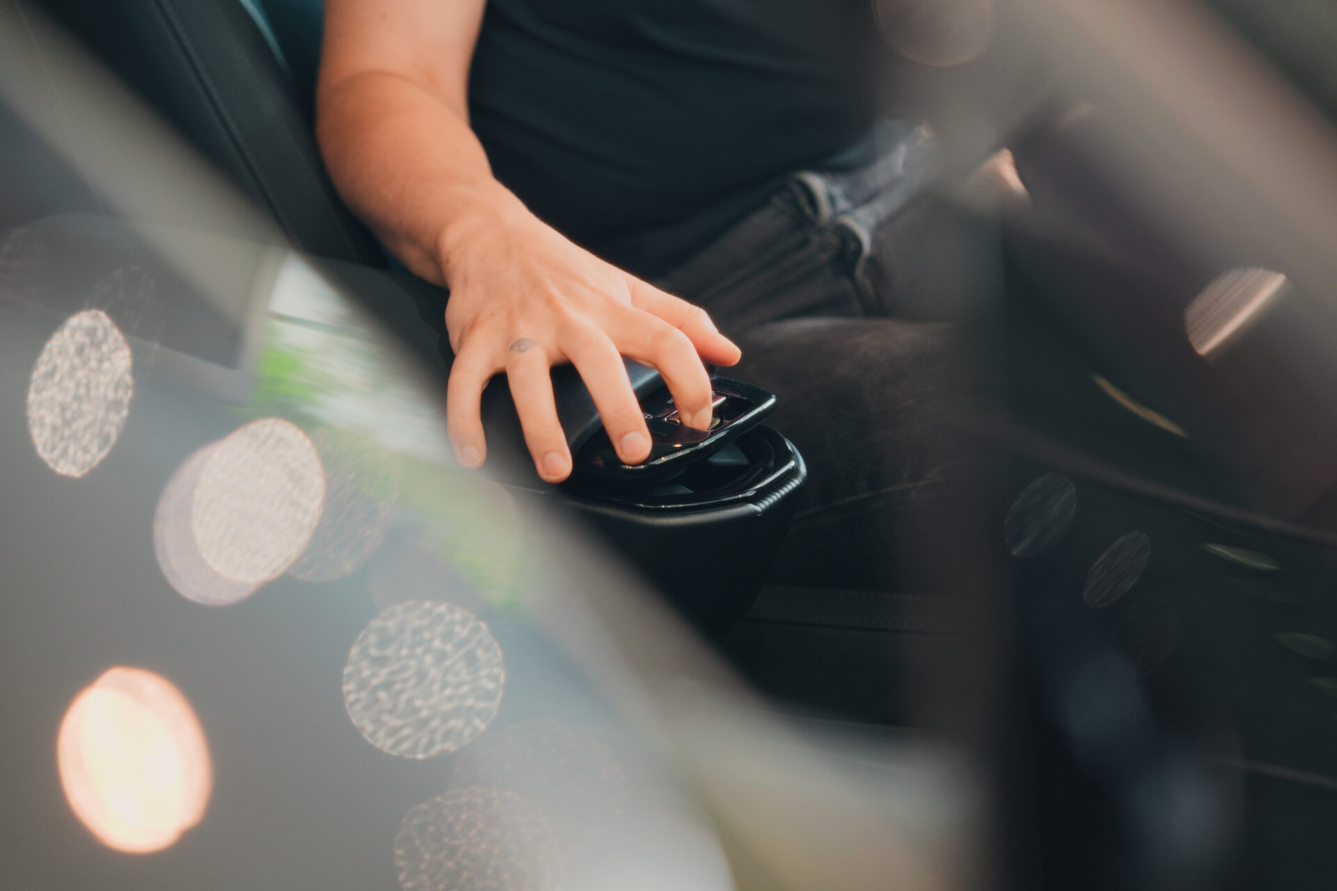 Närbild på en persons hand som vilar på Volvos centrala kontrollpanel inuti bilen med mjuka bokehreflektioner i Helmia i Arvika