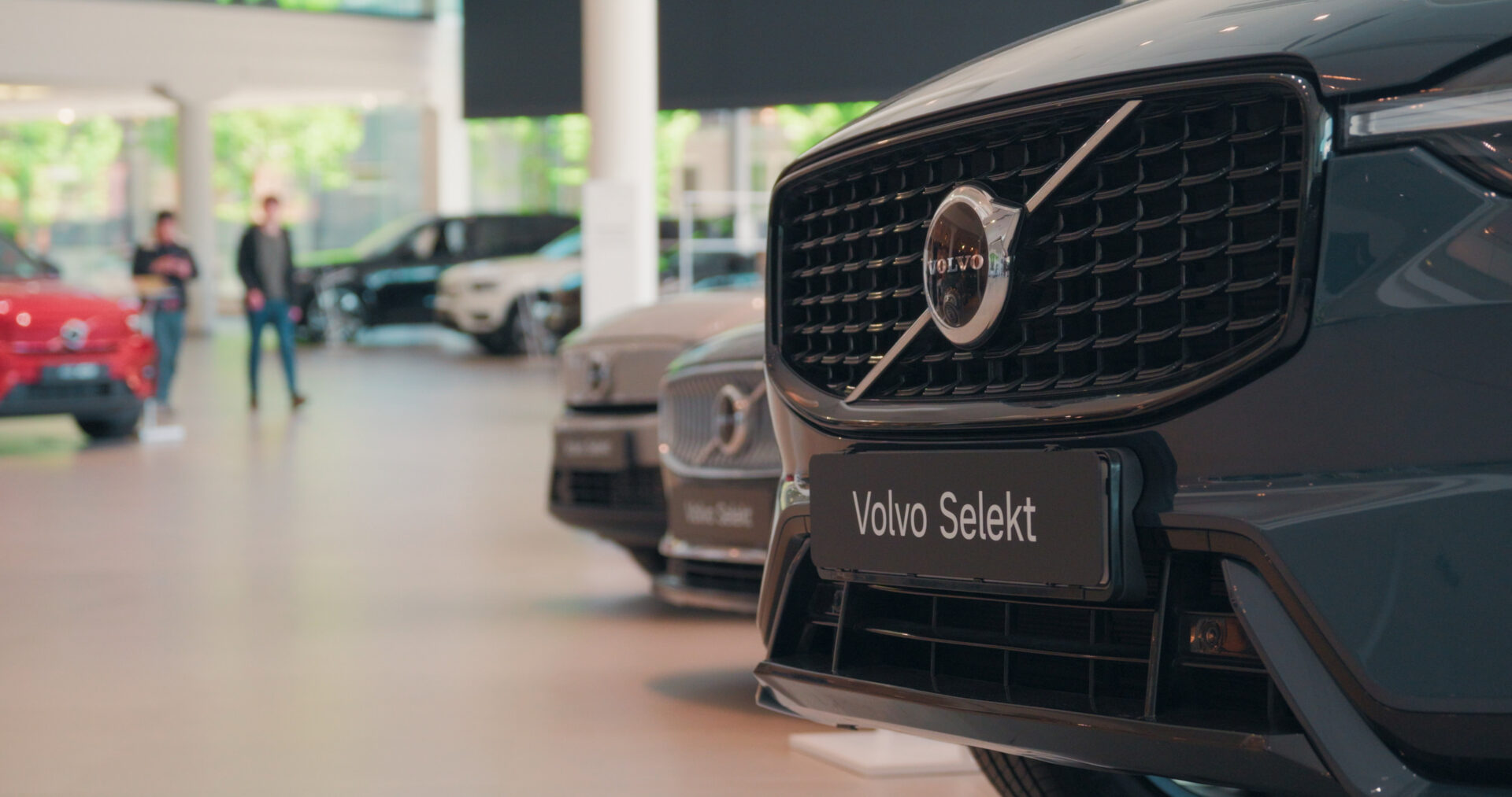 Närbild på Volvo Selekt frontgrill och logotyp med andra bilar suddiga i bakgrunden i Helmias bilhall