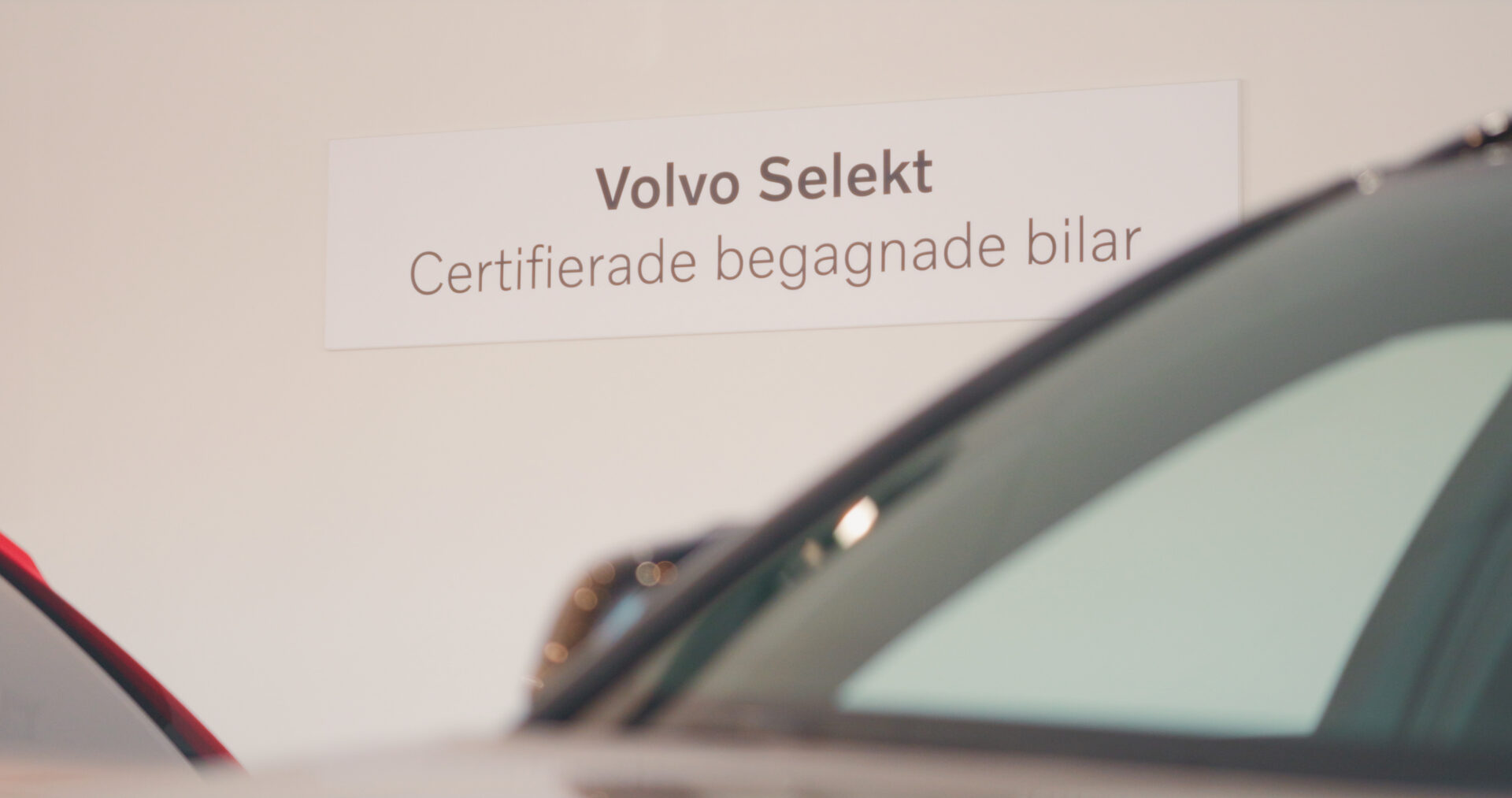 Helmia Volvo Selekt skylt med texten Certifierade begagnade bilar i bilhall med Volvo och fordon i förgrunden