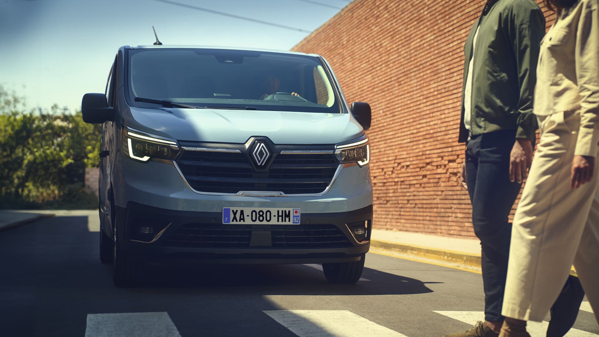 Renault Trafic E-Tech elbil parkerad på gata med röda tegelväggar och två personer som går över övergångsställe framför i Helmia